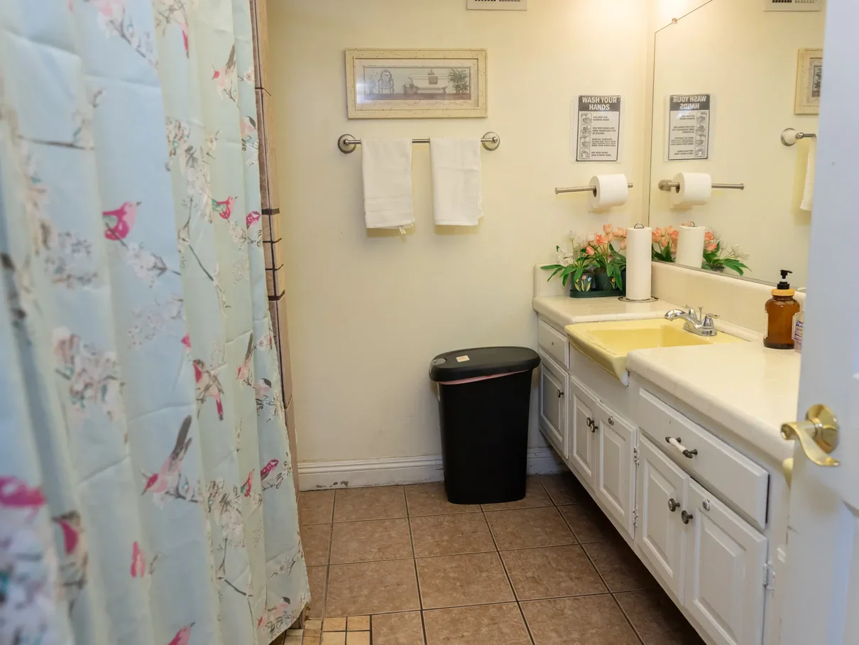 Accessible bathroom with safety features including grab bars, white vanity, and spacious layout suitable for senior care needs.
