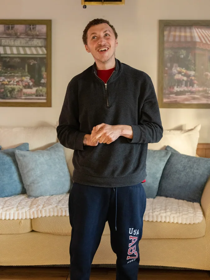 Resident smiling in comfortable living room setting with couch and decorative artwork.